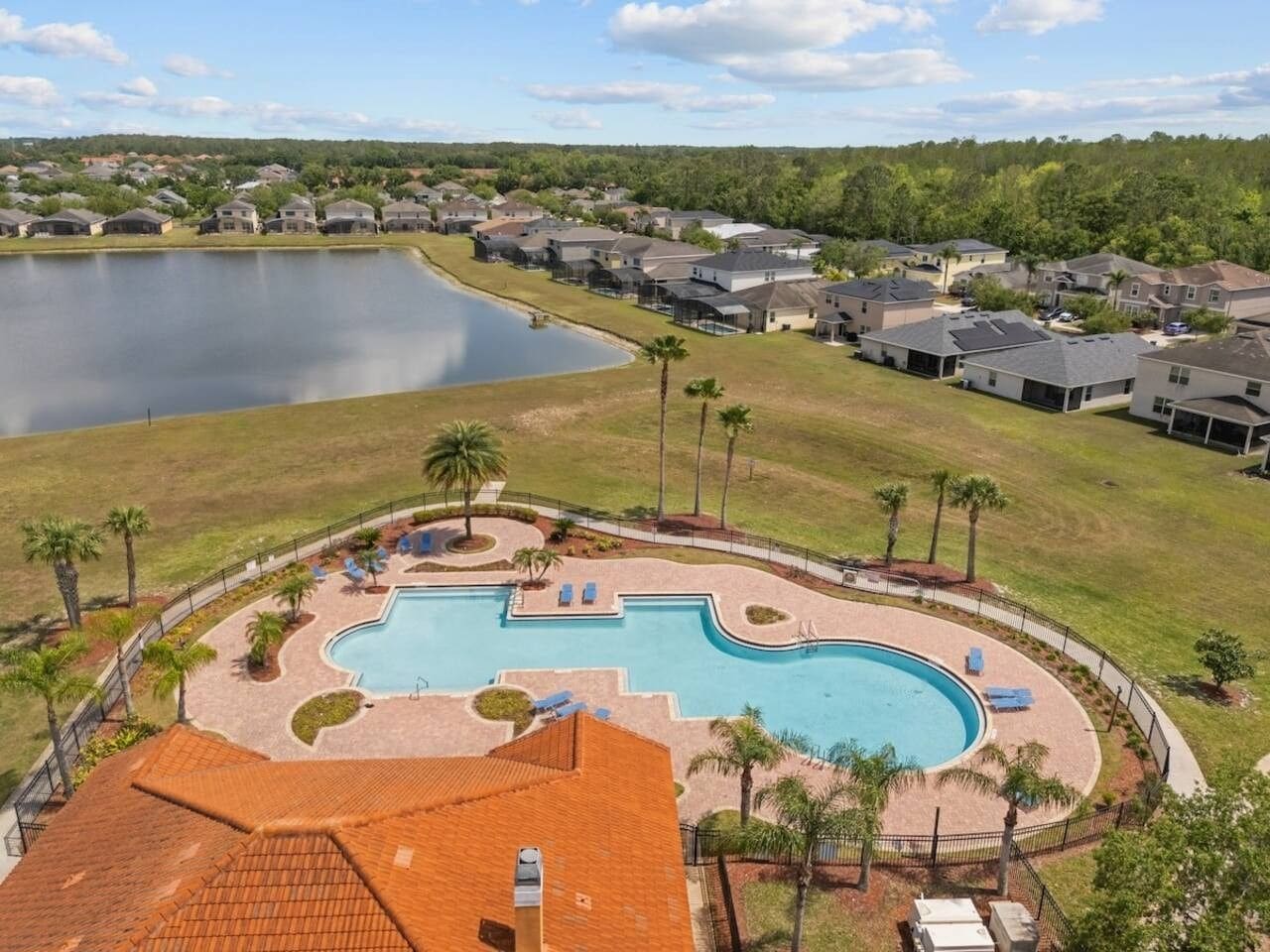 A residential area with a swimming pool surrounded by houses and a lake.