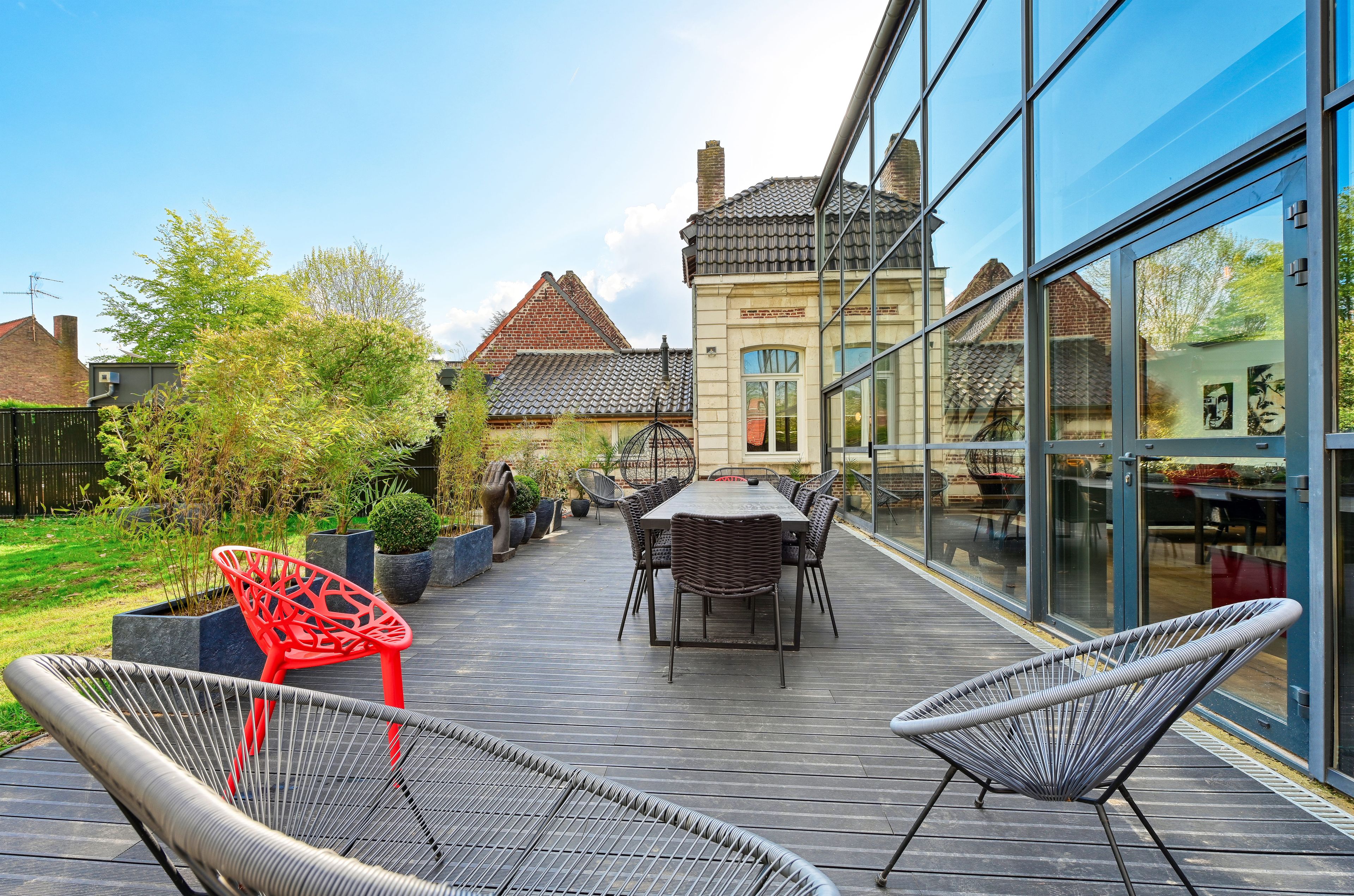 An outdoor patio with a dining table and chairs, surrounded by potted plants and a view of a traditional building.