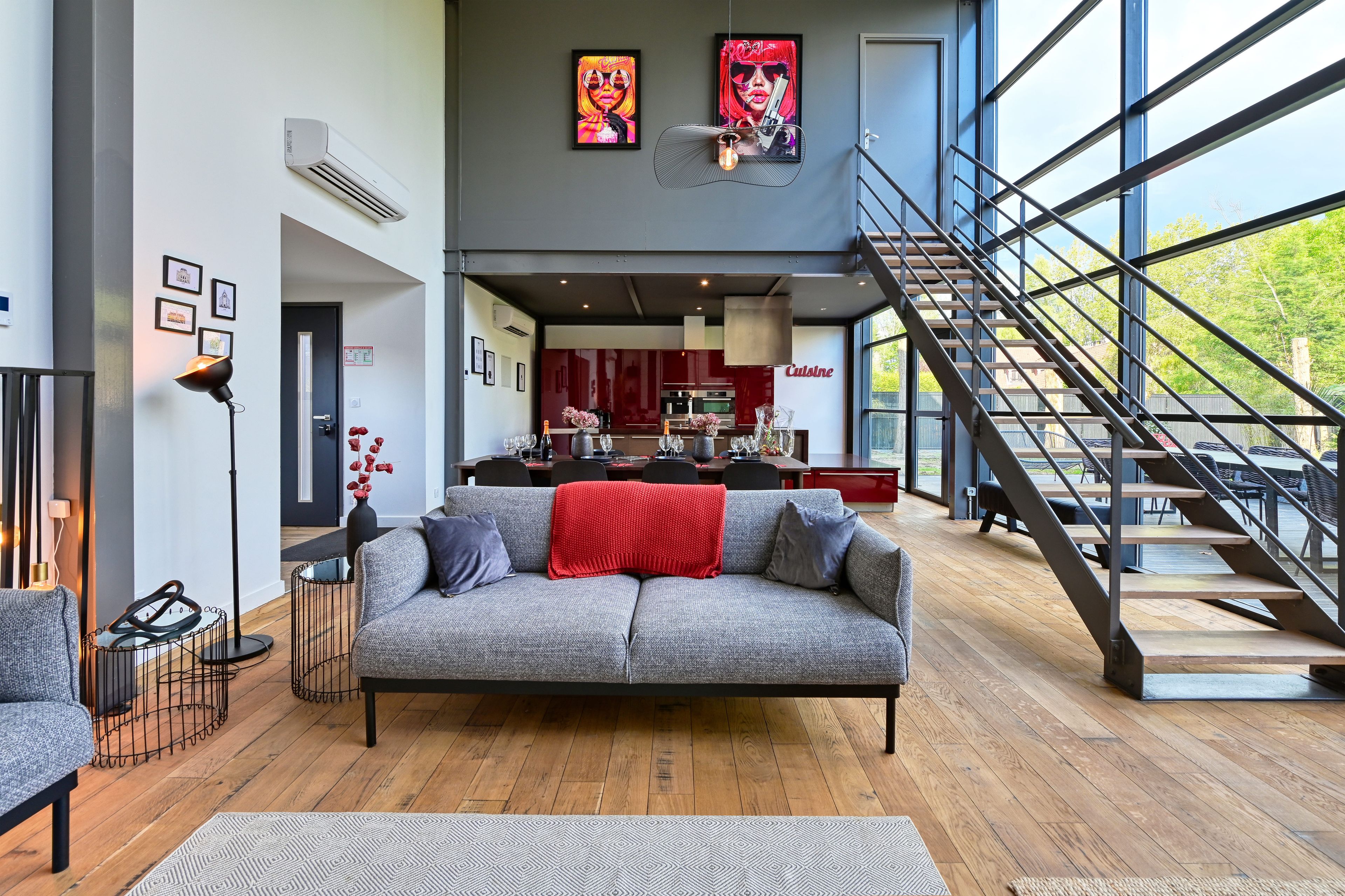 Ein modernes Wohnzimmer mit einem grauen Sofa, einer Treppe und einer Küche im Hintergrund.