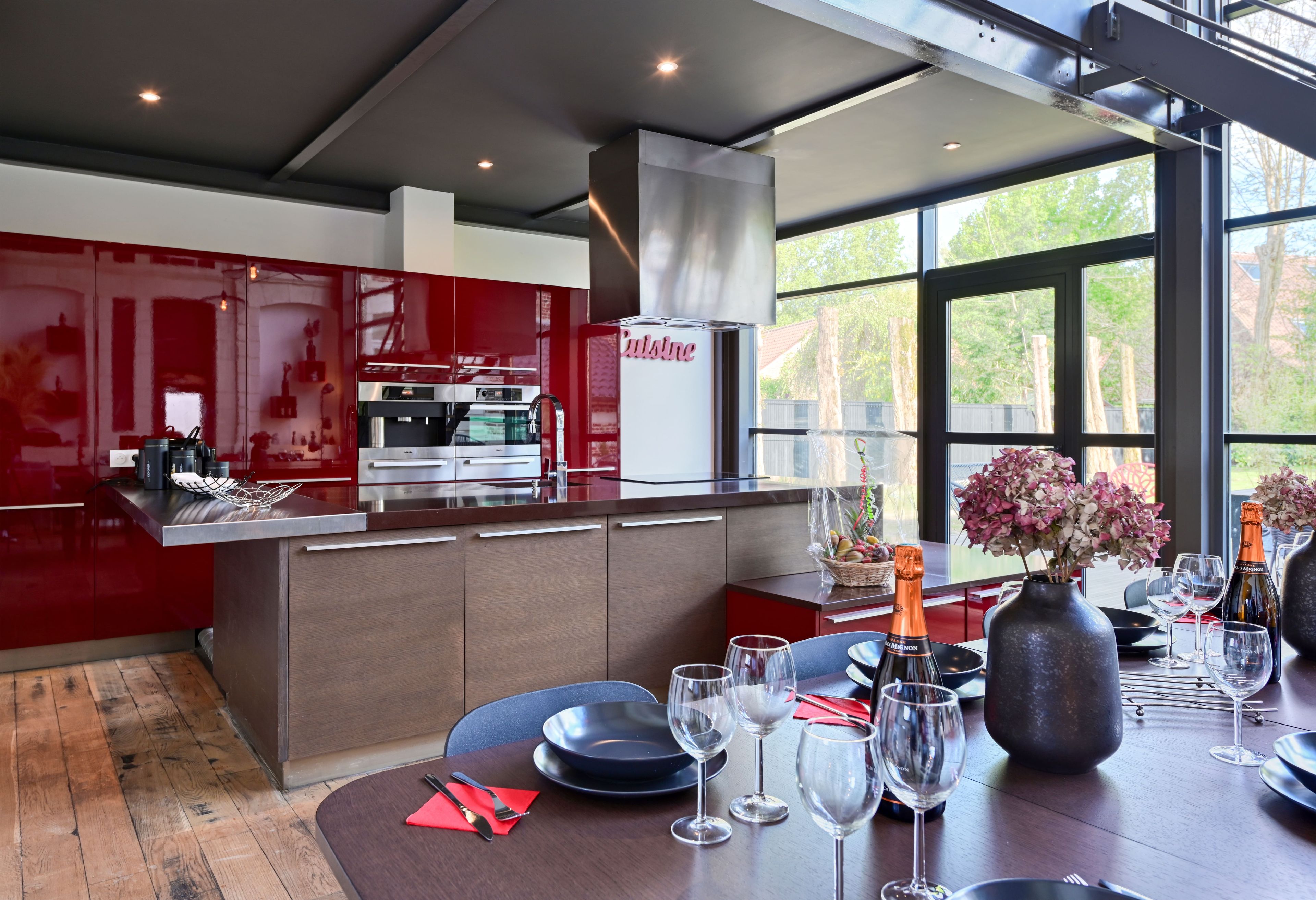 A modern kitchen with red cabinetry, stainless steel appliances, and a dining area with a table set for a meal.