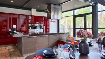 A modern kitchen with red cabinetry, stainless steel appliances, and a dining area with a table set for a meal.