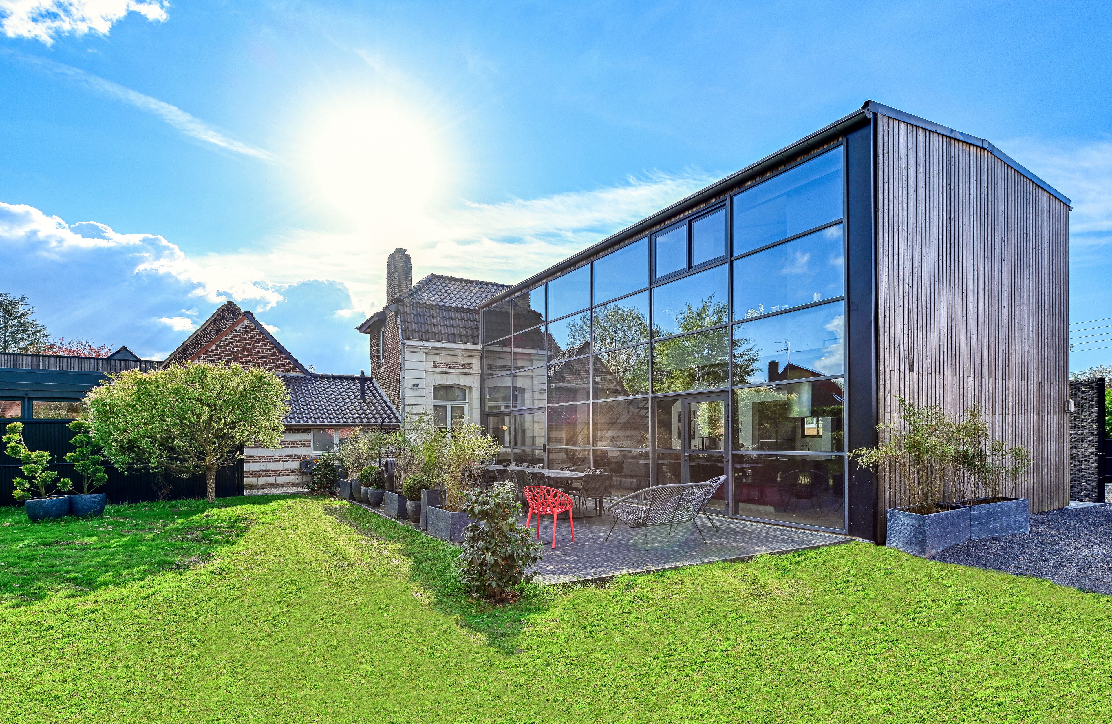 A modern building with large glass windows, a well-maintained lawn, and outdoor seating.