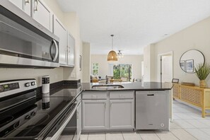 A modern kitchen with stainless steel appliances, a central island, and a view to the outdoors. - Retreat to Crystal Cove | Near Parks | Amenities (Kissimmee)