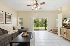 A living room with a grey sofa, a coffee table, a ceiling fan, and a television on a wooden cabinet. - Retreat to Crystal Cove | Near Parks | Amenities (Kissimmee)