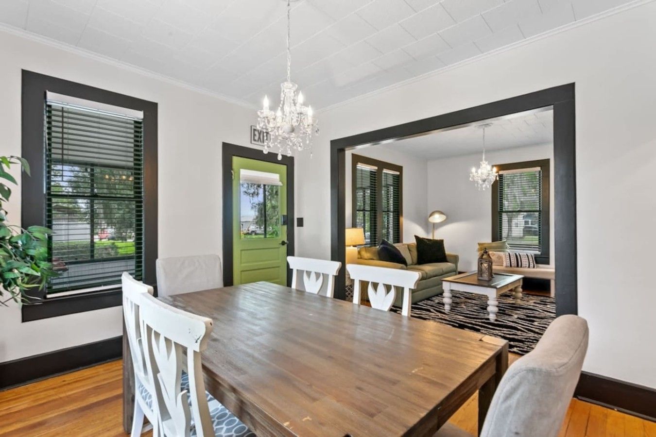 A dining area with a wooden table, white chairs, a chandelier, and a green door.