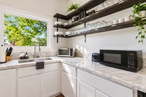 Una cucina moderna con mobili bianchi, forno integrato, microonde e una finestra con vista sugli alberi.