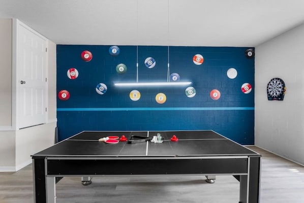 A room with a foosball table, a dartboard, and numbered billiard balls on the wall.