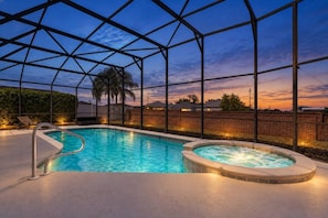 A swimming pool with a hot tub, surrounded by a covered area with a view of the sunset.