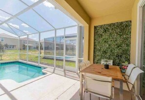 A covered outdoor area with a pool, a dining table with chairs, and a wall with a green leafy pattern. - Private Pool & Spa Villa | ChampionsGate (Kissimmee)