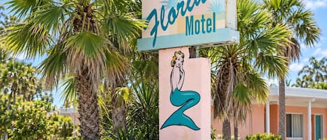 A Florida Motel sign with a stylized woman illustration, surrounded by palm trees and greenery.