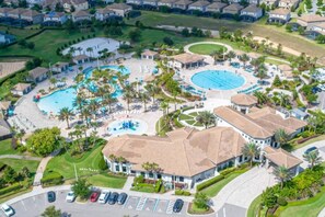 Vue aérienne d’un quartier résidentiel avec plusieurs piscines, une grande piscine centrale et un bâtiment doté d’un toit incurvé.