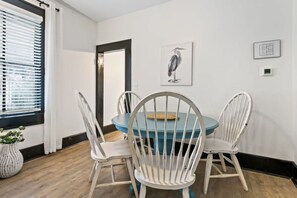 A dining area with a round table and four white chairs, a framed artwork on the wall, and a window with blinds. - St. Augustine Beach Getaway | Prime Location (St. Augustine)