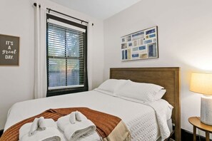 A hotel room with a bed, a window with blinds, a wall art piece, and a bedside lamp. - St. Augustine Beach Getaway | Prime Location (St. Augustine)