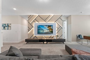 Ein modernes Wohnzimmer mit einem flachbildfernseher an einer Wand mit geometrischen Mustern, einer dunklen Unterhaltungsanlage und einem grauen Sofa.