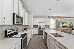 A modern kitchen with white cabinets, stainless steel appliances, and a large island with a sink. - SUPER DREAM – Luxury Poolside Loft | Pool & Games (Kissimmee)