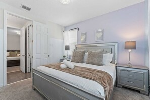 Ein Schlafzimmer mit einem Bett, Nachttischen, einer Lampe und einer Tür zu einem anderen Raum.