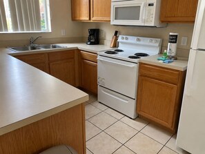 A kitchen with wooden cabinets, a white stove, a microwave, and a coffee maker. - Regal Palms Villa | Sliding Fun | Arcade | River (Davenport)