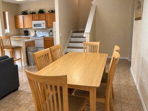 A compact living space with a dining table, chairs, a sofa, and a kitchen area with cabinets and appliances. - Regal Palms Villa | Sliding Fun | Arcade | River (Davenport)