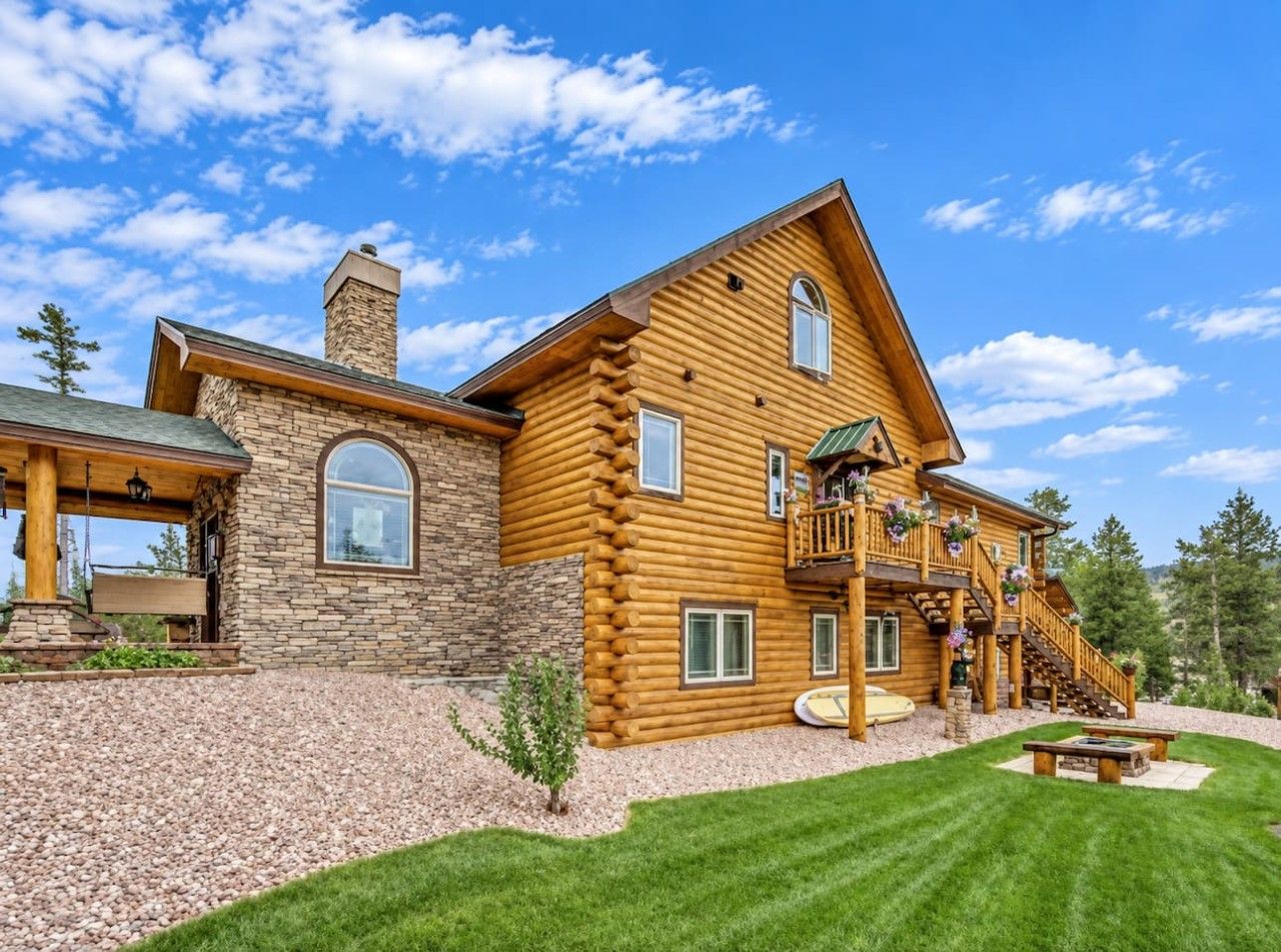 A large log cabin with a stone foundation, multiple windows, and a covered porch.