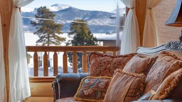 A cozy room with a wooden balcony, a cushioned sofa, and a view of snow-capped mountains.