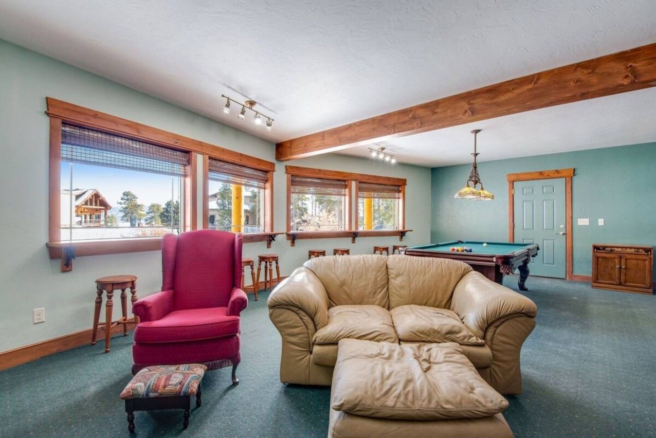 A spacious living room with a pool table, a red armchair, a beige sofa, and a large window with a view.