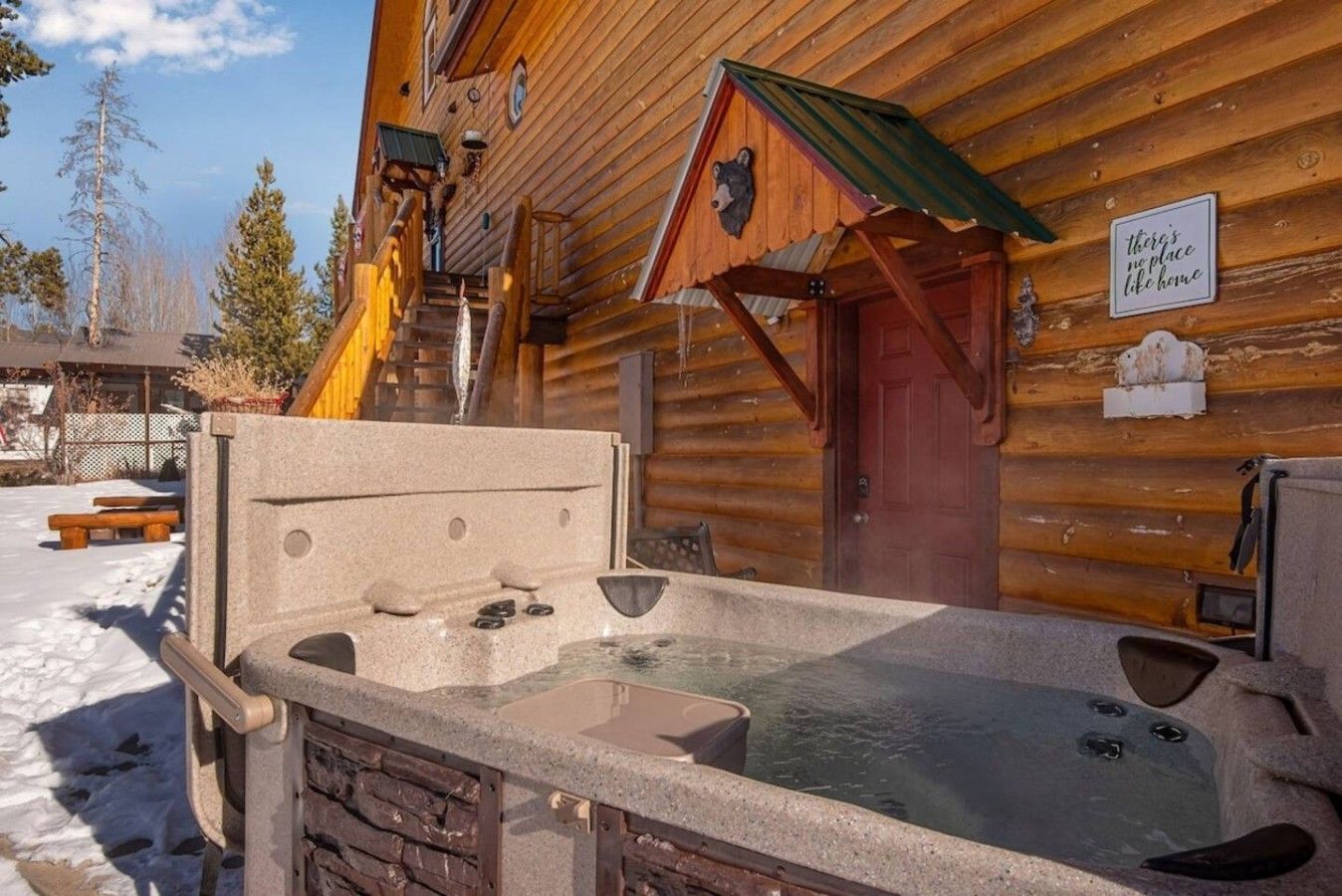 A wooden cabin with a hot tub and a wooden staircase leading to the entrance.