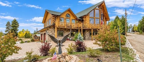 A two-story log cabin with a balcony, surrounded by a landscaped garden with a flag and an eagle statue.