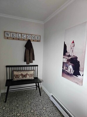 Una habitación con un banco, un cartel de 'WELCOME', un perchero y un cuadro colgado en la pared.
