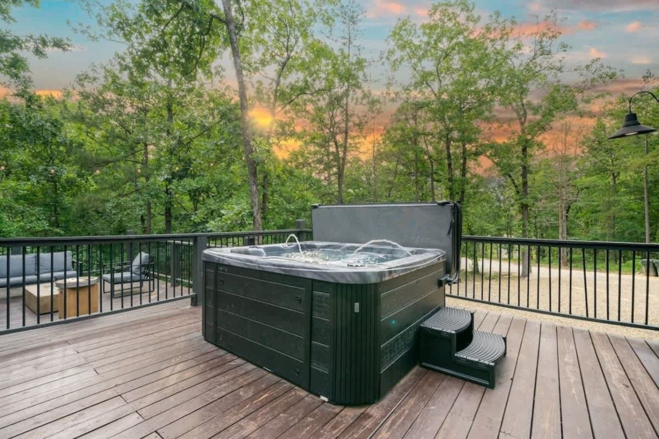 A hot tub on a wooden deck with a view of trees and a sunset.