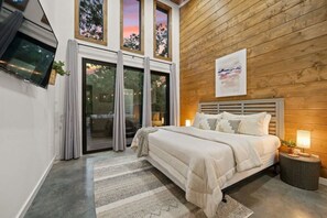 A bedroom with a bed, a TV, a window, and a wooden wall. - Secluded Oklahoma Cabin | Hot Tub & Private Acres (Broken Bow)