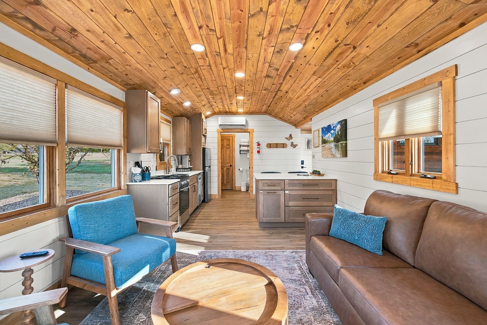 Un espacio habitable compacto con kitchenette, comedor y zona de estar con sofá y sillones.
