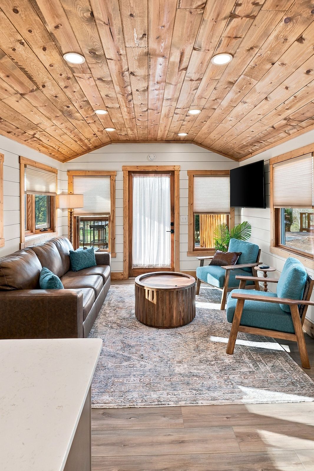 A spacious living area with a wooden ceiling, a brown leather sofa, a round wooden coffee table, and a blue armchair.