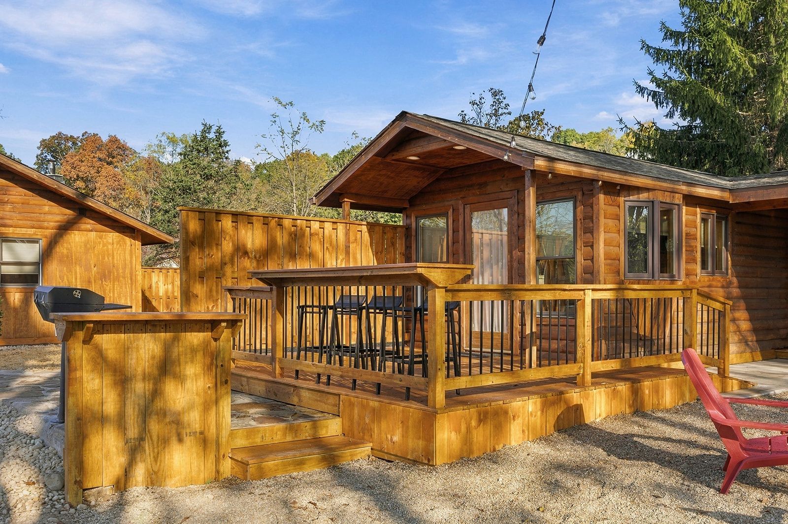A wooden cabin with a deck, outdoor seating, and a barbecue grill.