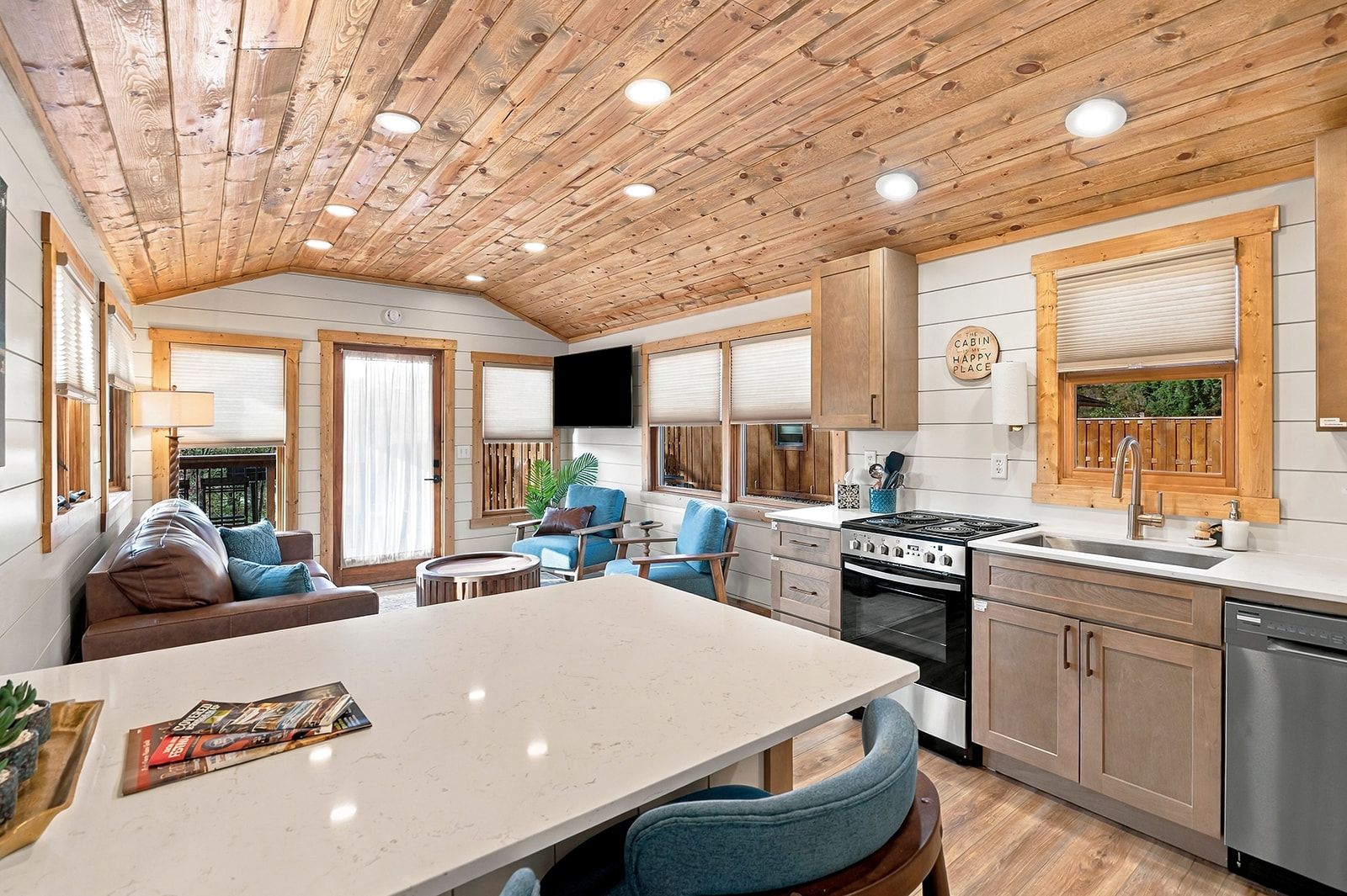 A cabin interior with a kitchen, dining area, and a living room with a sofa and chairs.