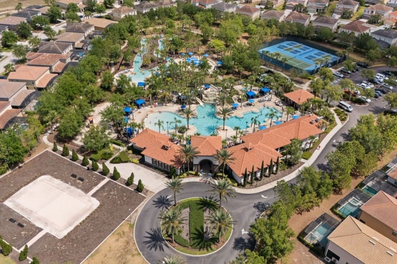 Vista aérea de un complejo turístico con múltiples piscinas, cancha de tenis y zona ajardinada con palmeras.