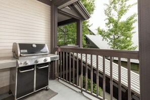 Una griglia per barbecue su un balcone con vista su alberi e una casa vicina.