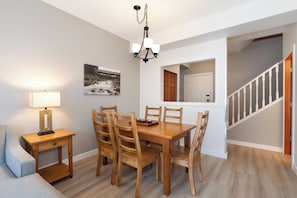 Un coin repas avec une table et des chaises en bois, un lustre, une lampe et un tableau au mur.