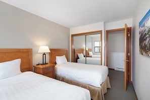 Una camera d'albergo con due letti, un comodino con una lampada, uno specchio e una porta che dà su un'altra stanza.