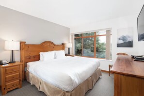 Habitación de hotel con una cama grande, cabecera de madera, lámparas de noche, un escritorio y una ventana con vistas a árboles.