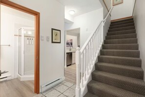 Una scala conduce a un secondo piano, una zona doccia con porta in vetro e una cucina visibile attraverso una porta aperta.