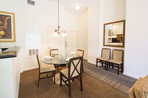 A dining area with a round glass table, four chairs, a chandelier, and a mirror on the wall. - Buena Vista Resort Village & Spa - Top Amenities (Orlando)