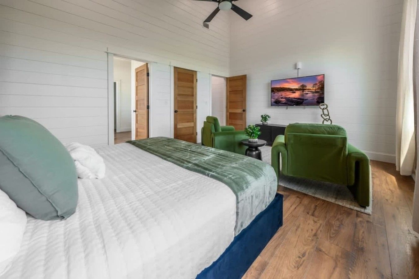 Een slaapkamer met een bed, een groene fauteuil, een klein tafeltje en een schilderij aan de muur.