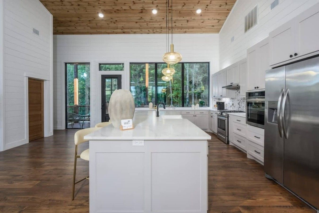 A modern kitchen with a central island, stainless steel appliances, and large windows offering a view of the outdoors.
