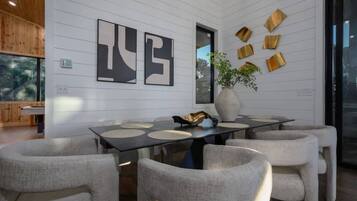 Un espace de salle à manger moderne avec une longue table, six chaises, des œuvres d’art abstraites accrochées au mur et un vase avec une plante.
