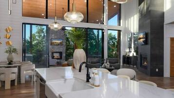 Une cuisine moderne dotée d’un grand îlot central, d’une cheminée en pierre et de grandes fenêtres offrant une vue sur l’extérieur.