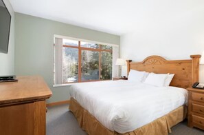 Una camera da letto con un letto, un comodino, una lampada e una finestra vista alberi.
