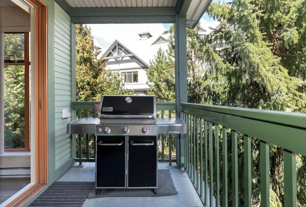 Una griglia per barbecue su un balcone con vista su una casa e alberi.