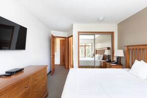 Une chambre d’hôtel comprenant un lit, une commode en bois, un téléviseur fixé au mur, une table de chevet avec une lampe et une porte coulissante donnant sur un balcon.