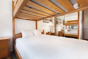 Un dormitorio con techo de madera, una cama con ropa de cama blanca, dos mesitas de noche con lámparas y una ventana con vistas al exterior.