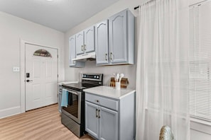 A kitchen with white cabinets, a stove, and a window with blinds. - Boho Lake Compound | 2 Homes + Waterfront (Kissimmee)